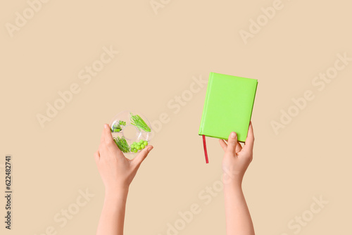 Female hands holding book and case with stationery on beige background