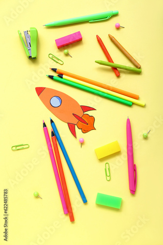 Paper rocket with school stationery on yellow background