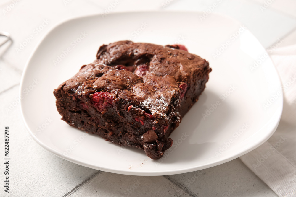 Plate with piece of raspberry chocolate brownie on white tile background Plate with piece of raspberry chocolate brownie on white tile background