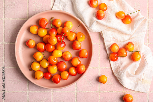 Plate with sweet yellow cherries on pink tile background