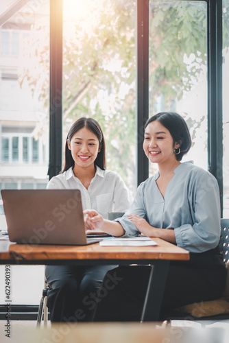 Two businesswoman working together on laptop computer. Creative female executives meeting in an office using laptop pc and smiling.