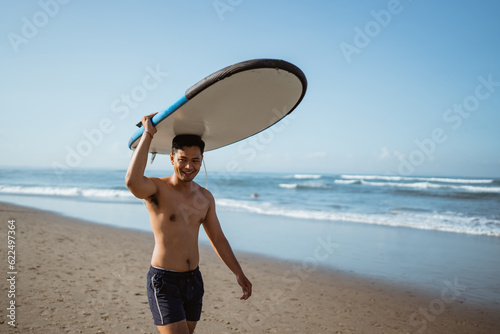 Photography Handsome Asian man with surfboard on his head walking along the beach enjoying v