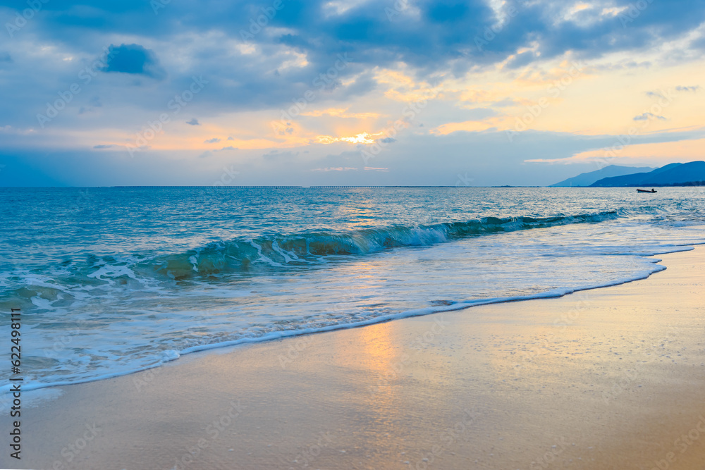 Sunset on the Sanya beach, the sun shines through the clouds on the golden sea and beach