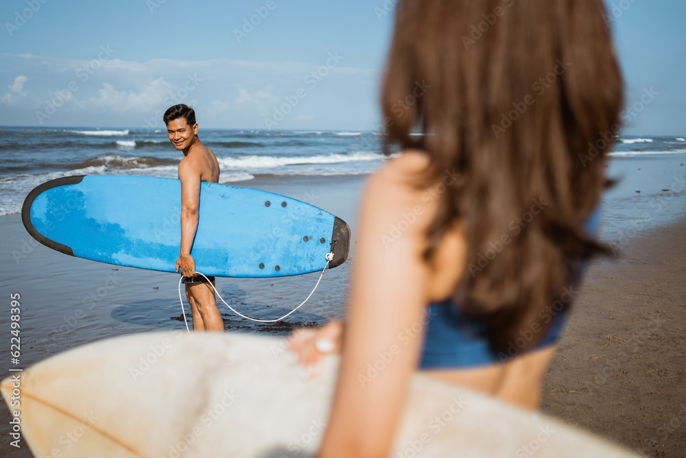 male surfer turns around with smile to see a beautiful female surfer with a surfboard on the beach