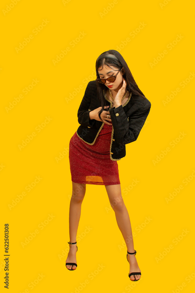 Fototapeta premium Fashion concept, Fashionable woman posing in mini red dress and black jacket on yellow background