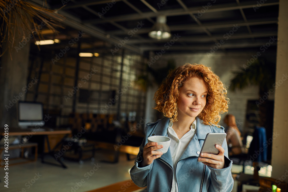 Young woman using a smart phone while looking through the window in a startup company office Young woman using a smart phone while looking through the window in a startup company office