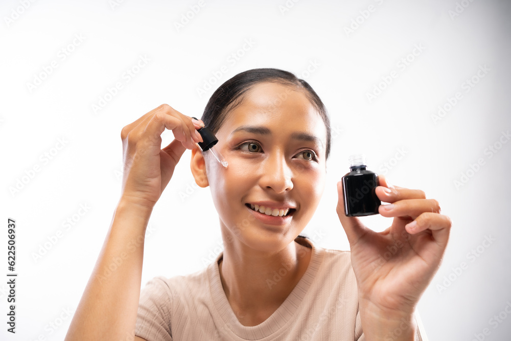 beautiful asian woman wearing cream t-shirt holding skincare ampoule serum smiling and looking sideways beautiful asian woman wearing cream t-shirt holding skincare ampoule serum smiling and looking sideways