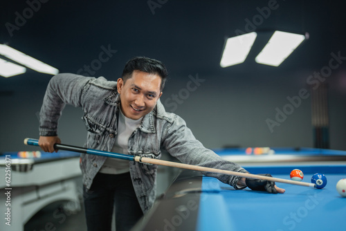 the male pool player smiling to the camera while standing and put her hands on the pool