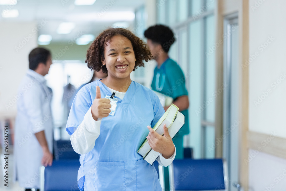 Portrait of woman medical student thumbs up holding school book have group students on background in classroom hospital medical school. concept of medical and education. Portrait of woman medical student thumbs up holding school book have group students on background in classroom hospital medical school. concept of medical and education.