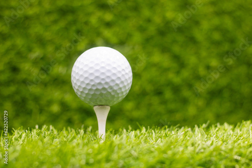 Golf ball is on tee with green grass background
