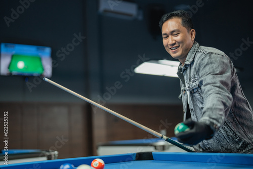 portrait of happy billiard player grabbing the ball and holding the cue stick