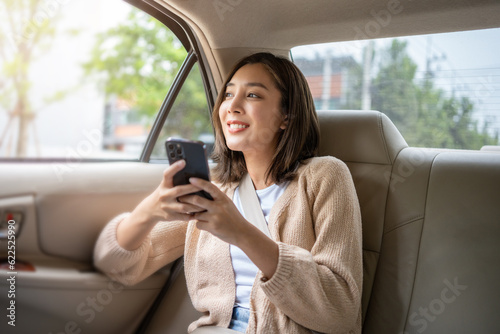 Billede på lærred Relaxing moment of beautiful woman sitting in car back seats using smartphone play social media with safety belt and look out the window