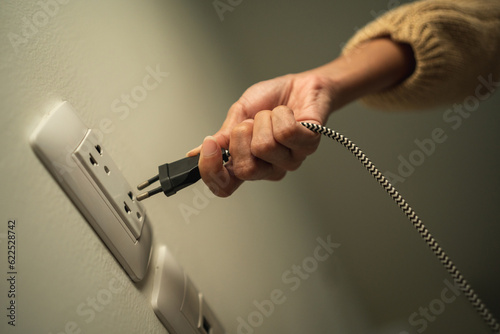 Close up woman hand put on or remove Electric plug cable in socket. Electrical equipment wires and power strips on the wall. Earth Hour saving energy.