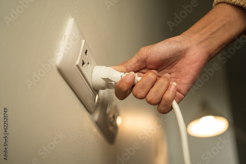 Close up woman hand put on or remove Electric plug cable in socket. Electrical equipment wires and power strips on the wall. Earth Hour saving energy.