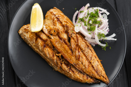 Baked mackerel fillets with lemon and onion on a black plate on dark wooden table, flat lay