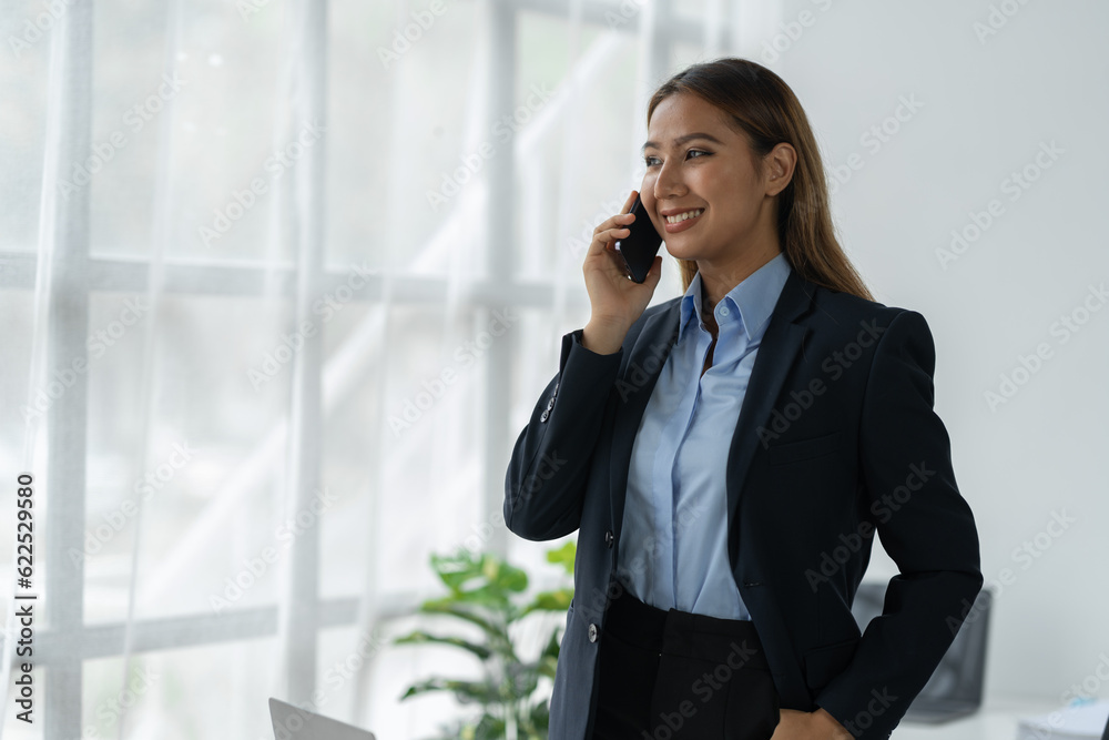 Happy Asian businesswoman talking on the phone and smiling while sitting at work using smartphone to talk. Contact via online application, concept of management Happy Asian businesswoman talking on the phone and smiling while sitting at work using smartphone to talk. Contact via online application, concept of management