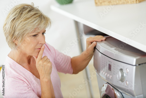 senior wash woman looking at washing machine photo