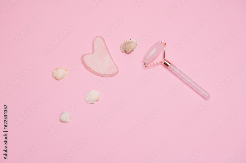 Quartz face roller massager and Gua sha stone scraper on isolated pink background, flat lay. Anti-aging treatment. Spa