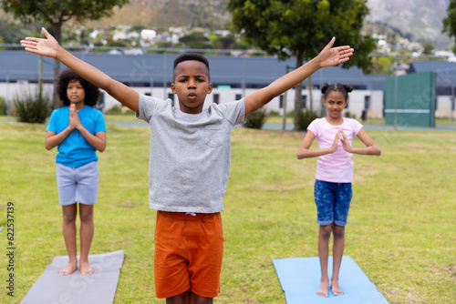 Happy african american schoolchildren doing yoga and meditating on field at school