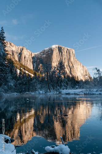 The rocky surface of the Sierra Nevada mountains  reflecting early morning sunlight  being reflected in Merced river  on an early winter  snow-covered landscape in Yosemite national park.