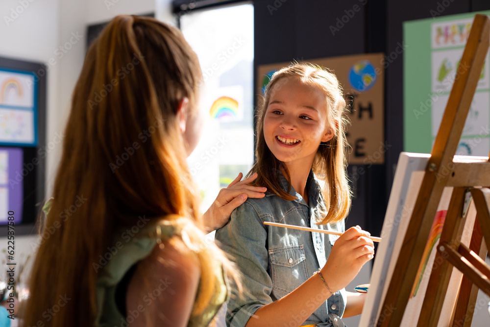 Fototapeta premium Happy diverse schoolchildren painting using brush and easel in school art class