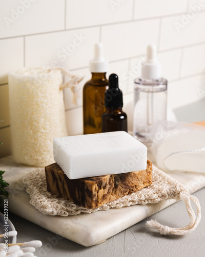 Handmade organic bar soaps on white tile background. Sustainable zero-waste lifestyle with serum bottles and bath accessories. Copy space for your text