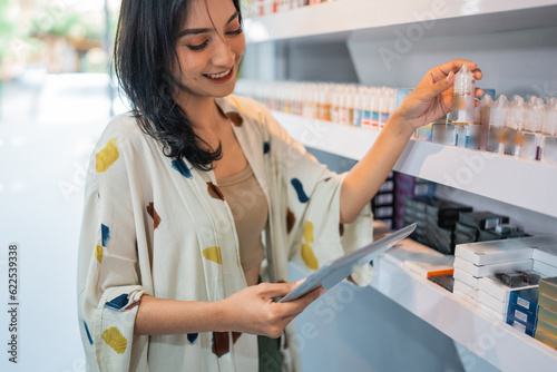 beautiful shopkeeper looking at the digital tablet while checking the liquid stock at the shelf photo