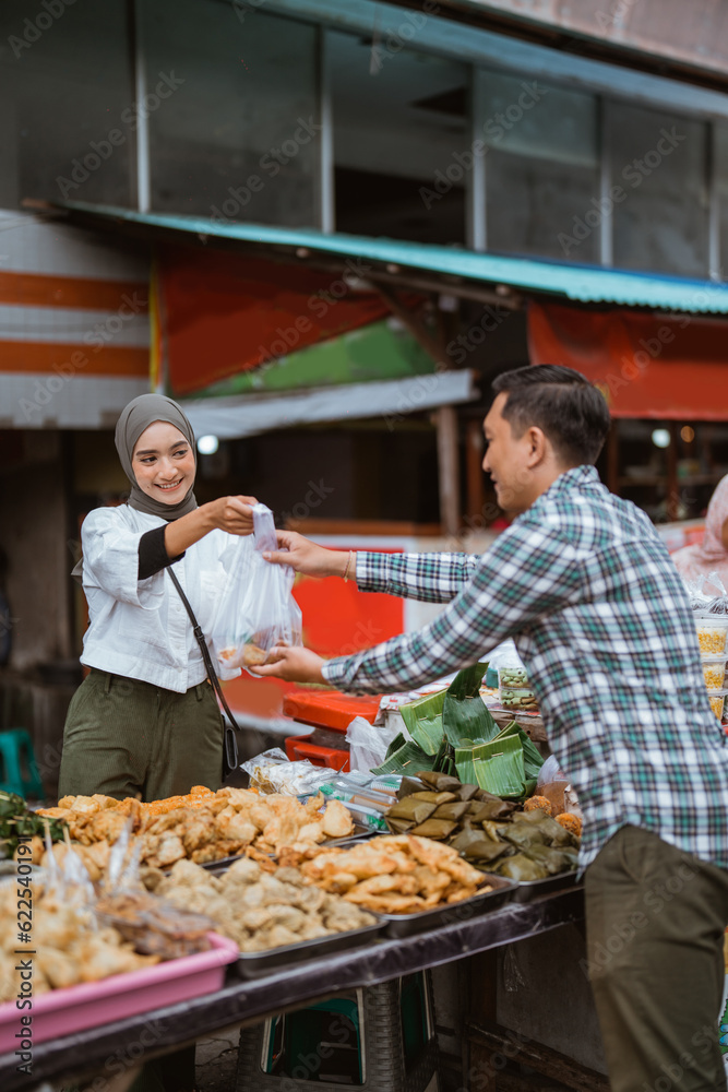 A beautiful girl wearing a headscarf selling a food stall on the side of the road gives takjil food to a buyer at the stall