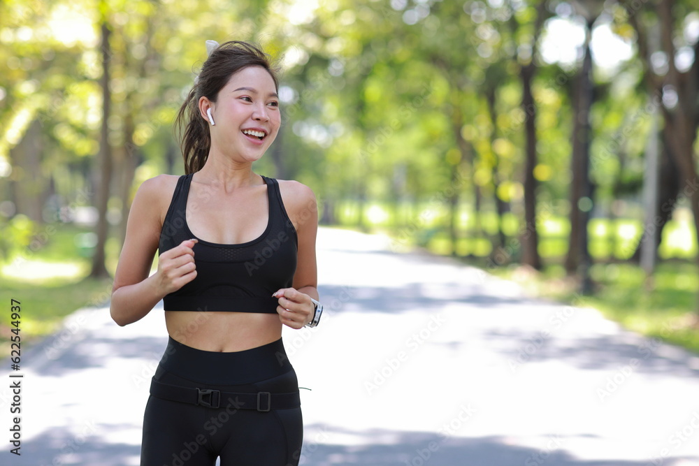 Beautiful asian fitness female sportswoman runner doing morning jogging exercise training outdoor. Happy smiling athlete woman running under the tree in the park while looking away and listen music. Beautiful asian fitness female sportswoman runner doing morning jogging exercise training outdoor. Happy smiling athlete woman running under the tree in the park while looking away and listen music.