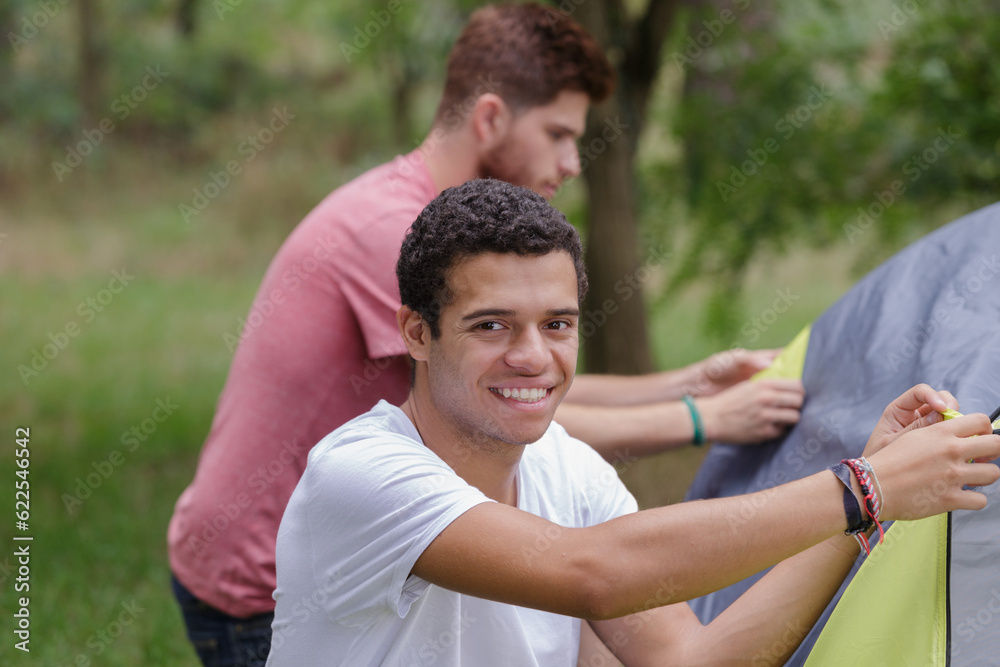 portrait of man making tent with friend in forest portrait of man making tent with friend in forest
