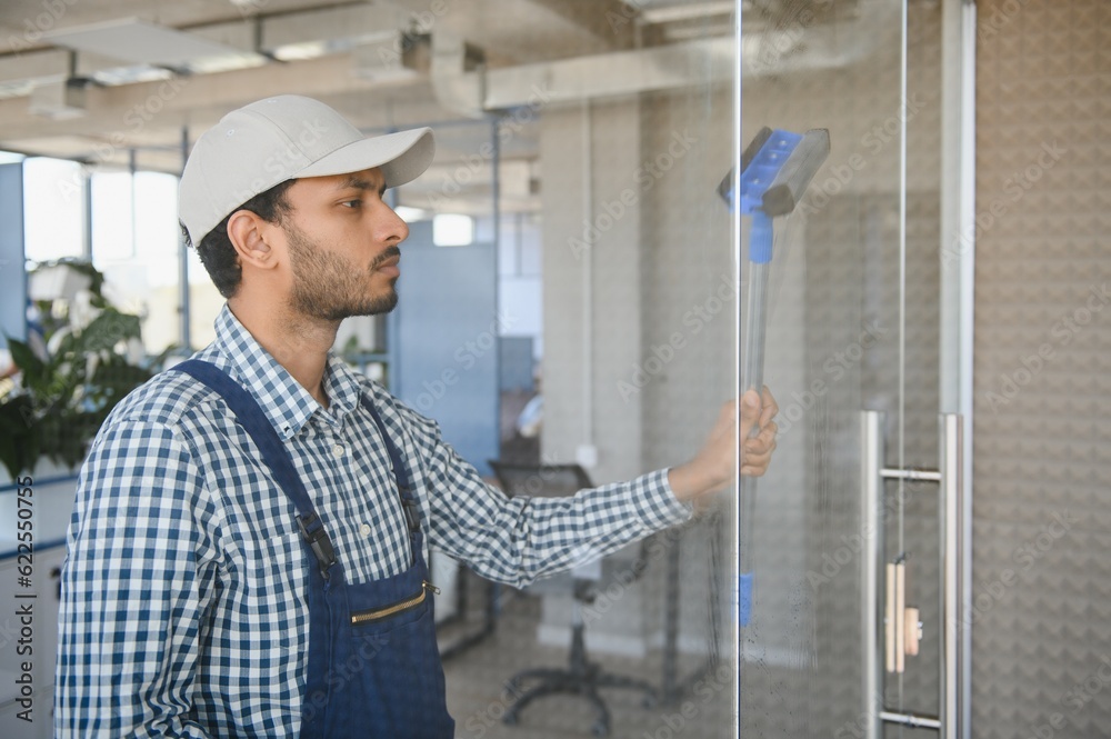 Young indian man washing window in office Young indian man washing window in office