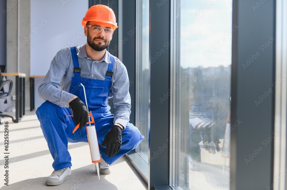 Workers with tube of sealant and suction lifters installing plastic windows indoors. Workers with tube of sealant and suction lifters installing plastic windows indoors.