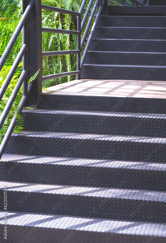 Sunlight and shadow on black metal staircase of natural skywalk in the garden at public park Sunlight and shadow on black metal staircase of natural skywalk in the garden at public park