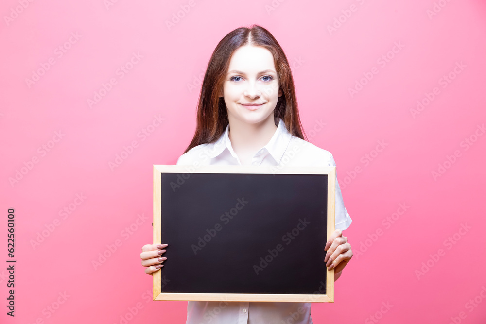 Student woman wearing White Shirt holding Black Board for Advertising Notes over isolated Pink background. Student woman wearing White Shirt holding Black Board for Advertising Notes over isolated Pink background.