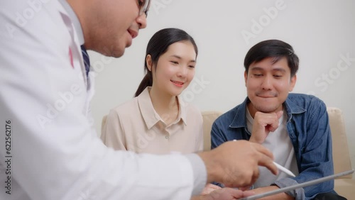 Male doctor giving test result to asian couple patient with tablet. They feeling happy and holding hand together when received good news from the doctor in medical office, hospital, clinic or home.