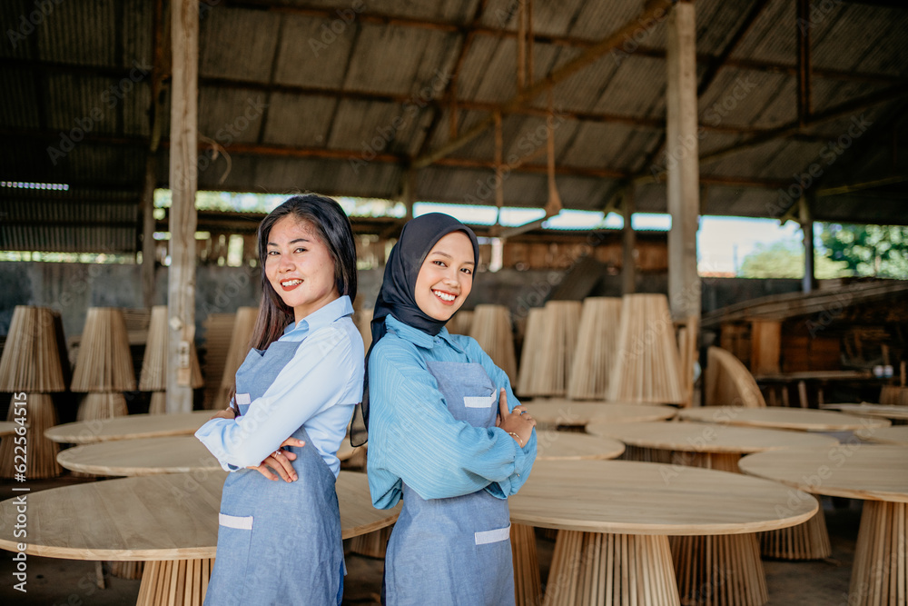 two female entrepreneurs stand back to back with crossed hands at a woodcraft shop