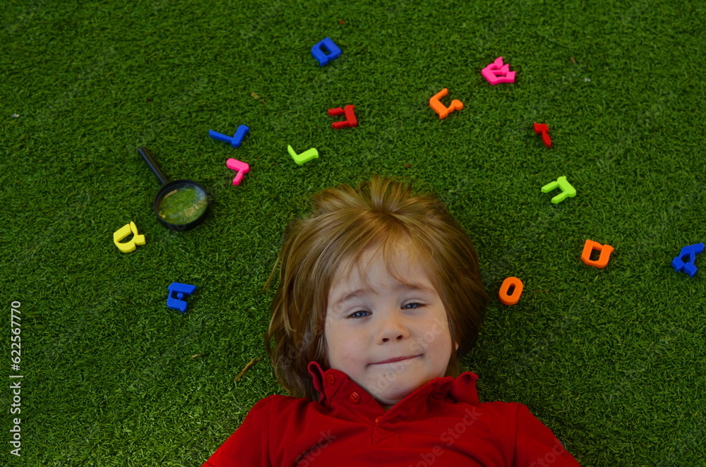 Hebrew alphabet. The boy is learning Hebrew. Multicolored letters on the grass. The child is