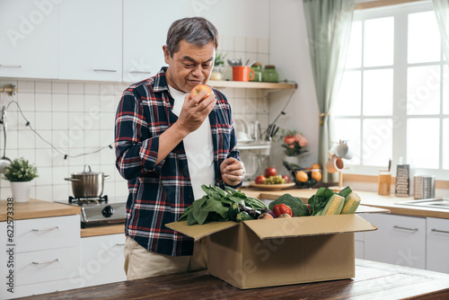 The retired Asian man enjoyed the convenience of online shopping as he unpacked a carton box filled with healthy vegetable ingredients on his dining table.