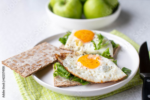 Gluten free and vegetarian breakfast plate with low carb cripbread, arugula, fried eggs and green apples on white background