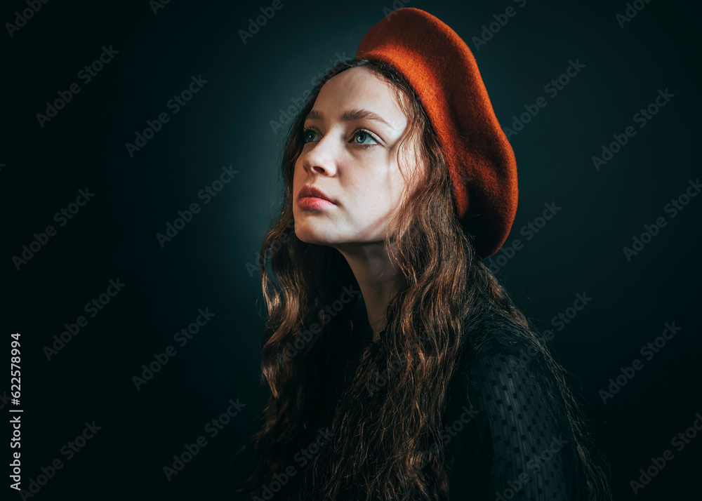 Fototapeta premium Portrait of a sad young woman in an orange beret and long curly hair on a dark background.