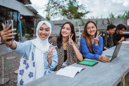 three female college students selfies using cell phones while using a laptop at an outdoor cafe