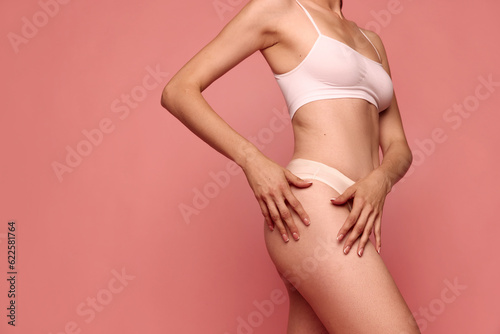 Cropped image of slim, healthy female body, legs against pink studio background. Model posing in underwear. Anti cellulite care. Concept of female beauty, body care, fitness, sport, health, figure, ad
