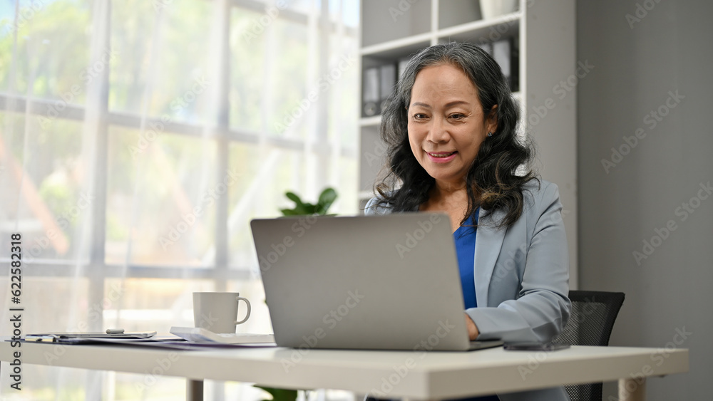 A smiling Asian senior businesswoman working on her business work on her laptop A smiling Asian senior businesswoman working on her business work on her laptop
