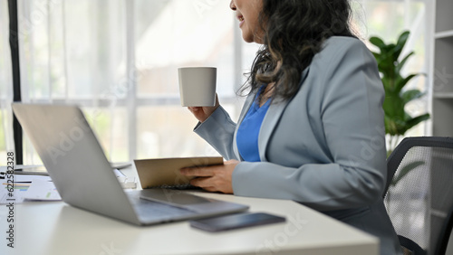 A senior businesswoman sipping coffee while working on her business work at her desk.