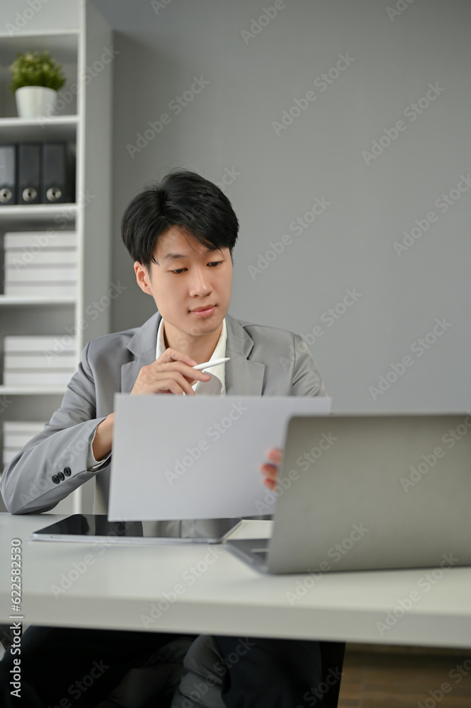 A smart and focused Asian businessman reading a document at his desk in the office. A smart and focused Asian businessman reading a document at his desk in the office.