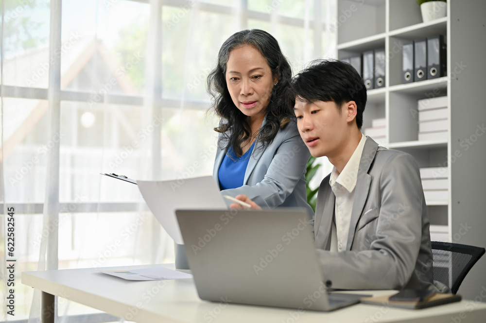 An Asian senior female boss is co-working on a new project with a young male worker An Asian senior female boss is co-working on a new project with a young male worker