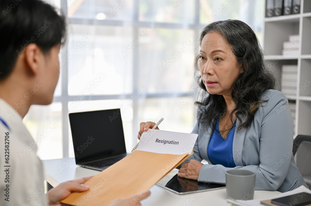 A young Asian male office employee giving a resignation letter to a female boss A young Asian male office employee giving a resignation letter to a female boss