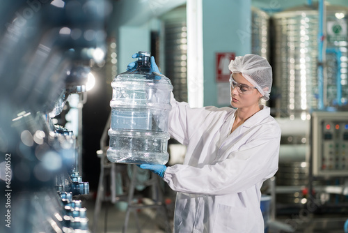 Female worker produces inspecting quality of plastic drinking water tank in mineral water plant. Factory female worker working and checking plastic gallon during manufacturing water bottling process