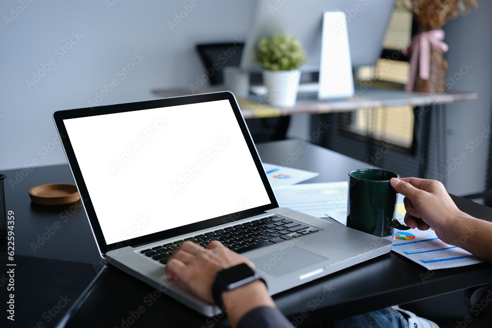 Closeup young businessman holding coffee cup and using laptop computer on black office desk Closeup young businessman holding coffee cup and using laptop computer on black office desk