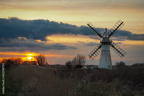 Beautiful orange sunset lighting up the clouds over Thurne Dyke Drainage Mill set in The Broads, near Great, Yarmouth, Norfolk, UK photo